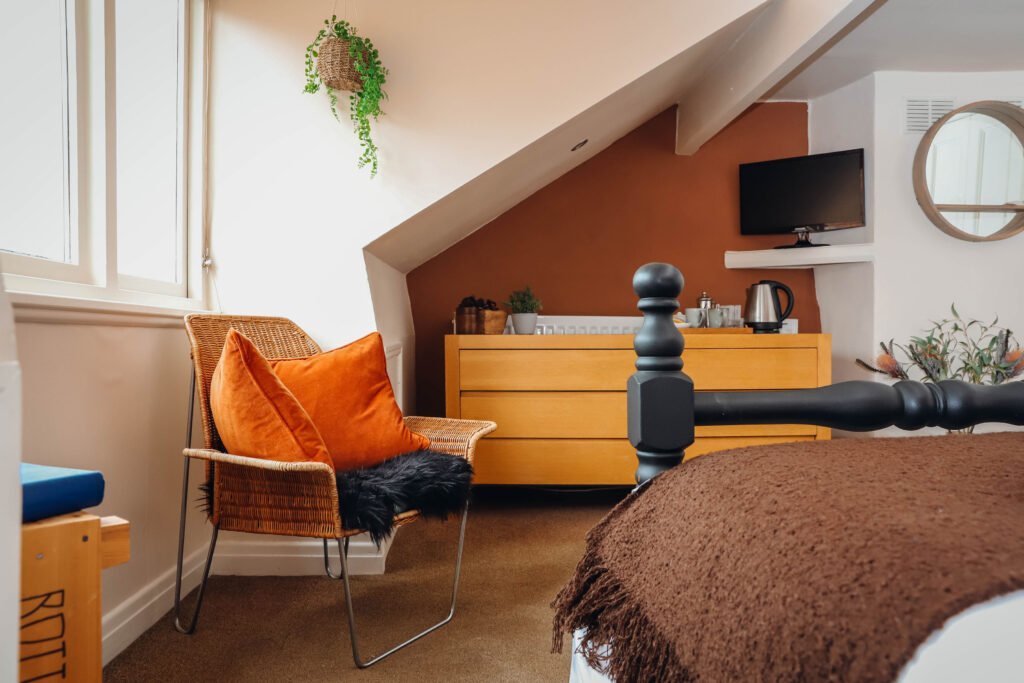 A cosy bedroom with chair by the window and TV in the corner.