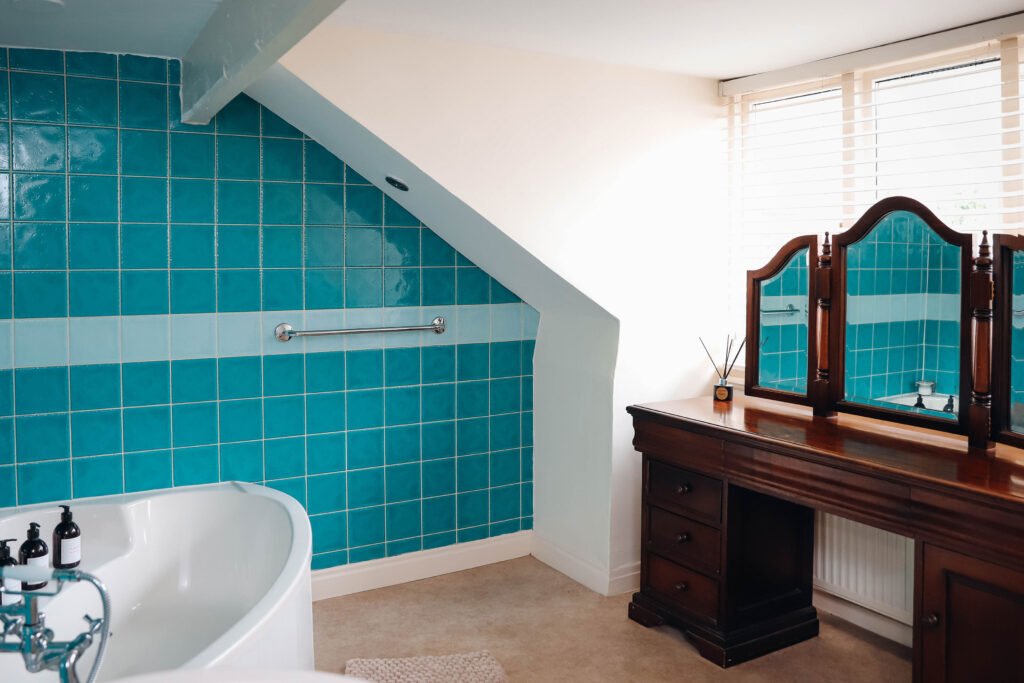 A white bath in a blue bathroom with a dressing table by the window.