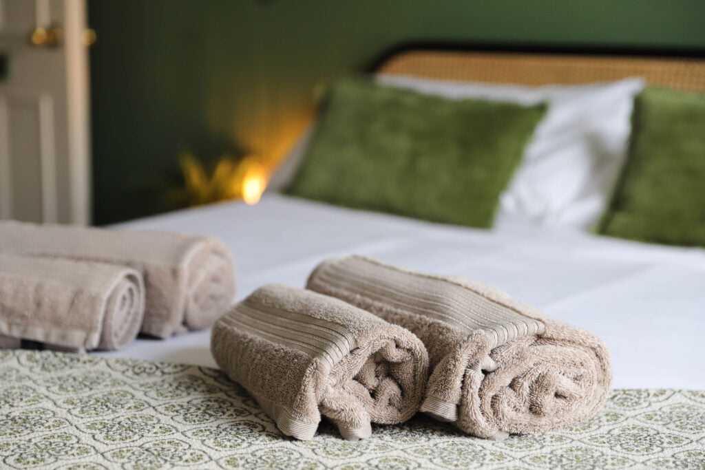 Beige towels neatly rolled onto a bed with green bedding.
