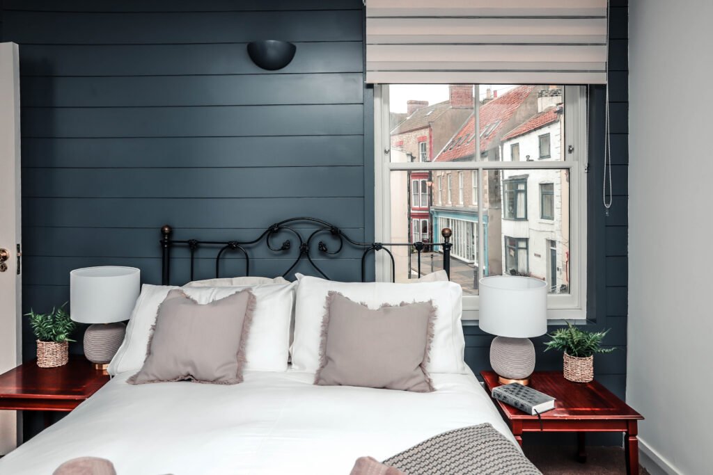 A comfortable bedroom with grey pillows and a view out of the window over the town.