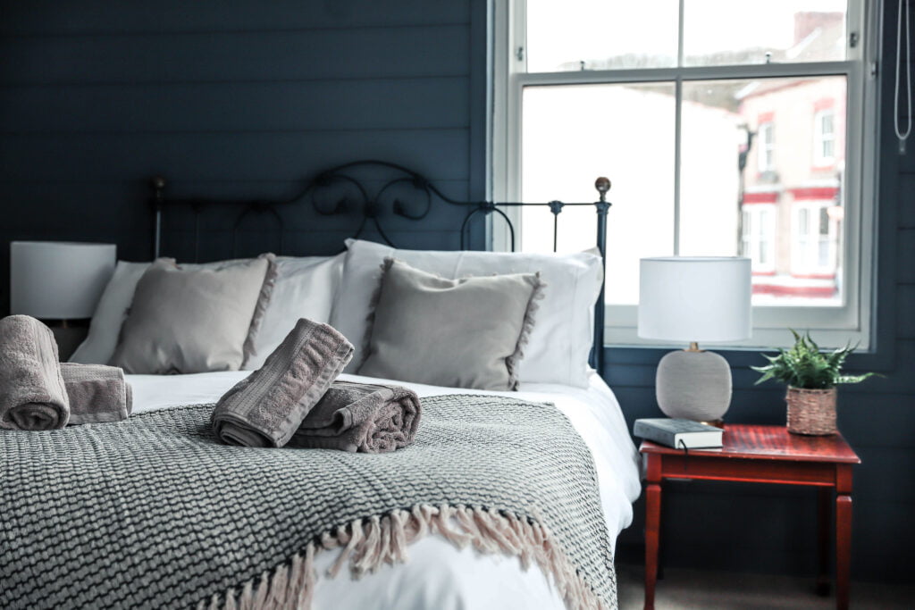 A cosy bedroom with grey towels neatly folded on top of the bed with a view out of the window.