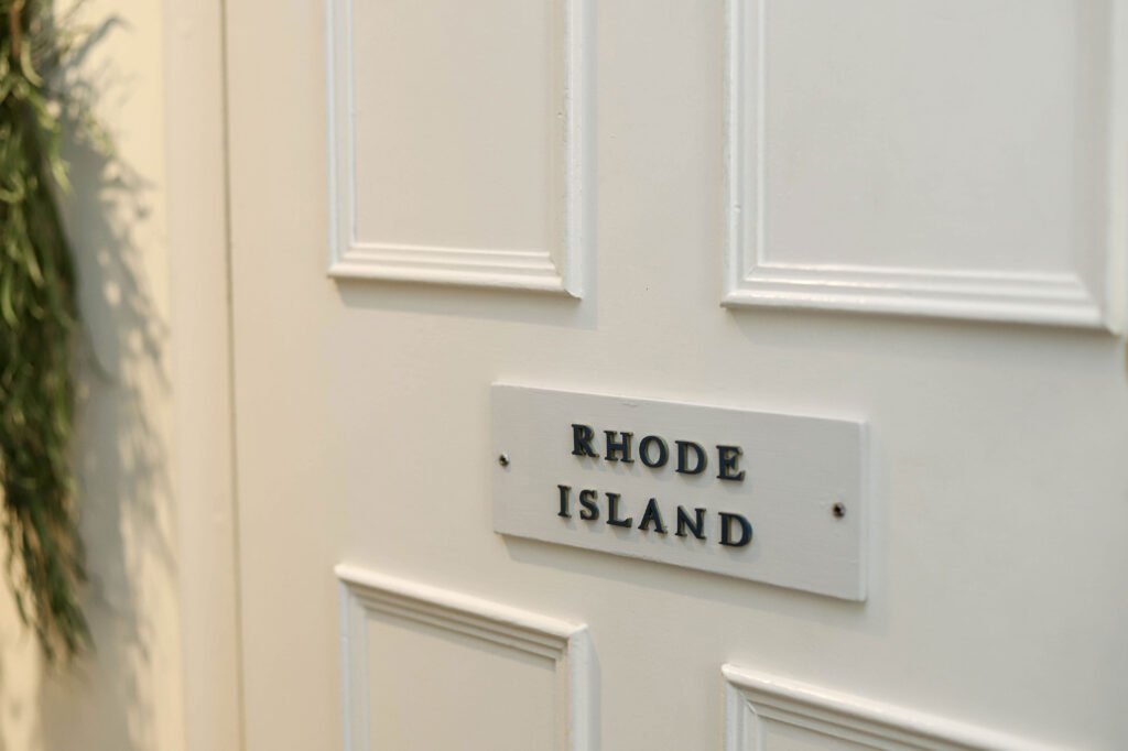 A white sign on a white door which reads 'Rhode Island' in black text.